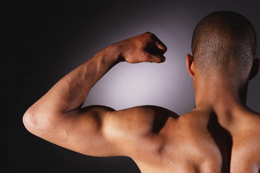 Man flexing bicep muscle from back view illustrating arm strength and anatomy relevant to bicep tenotomy procedure
